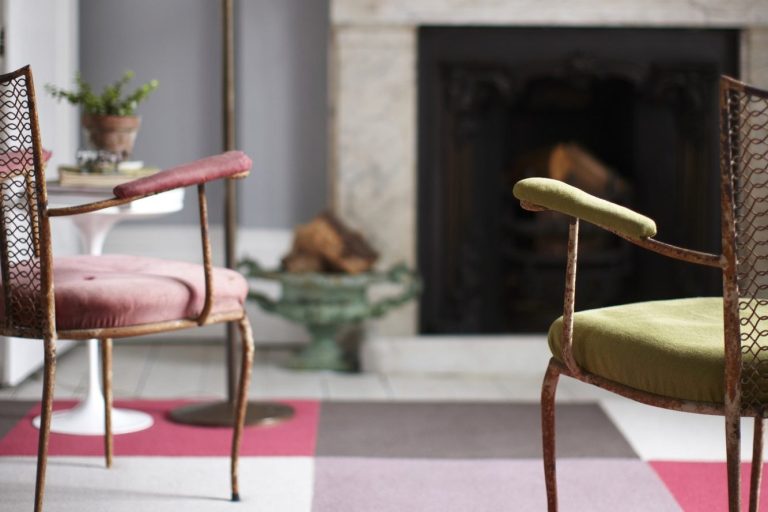 Roger Oates pink and grey floor textiles beneath two upholstered chairs beside a fireplace.
